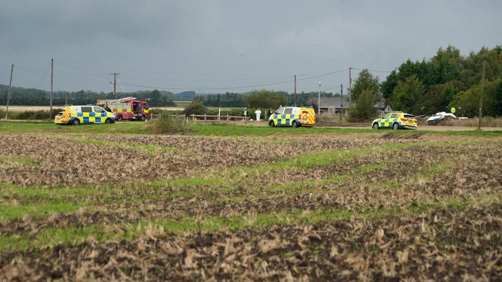 Image shows a field in which police vehicles, an ambulance and a fire engine can be seen.