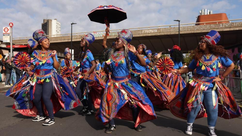 Performers in blue and multicoloured costumes dance along a carnival route during Family Day.
