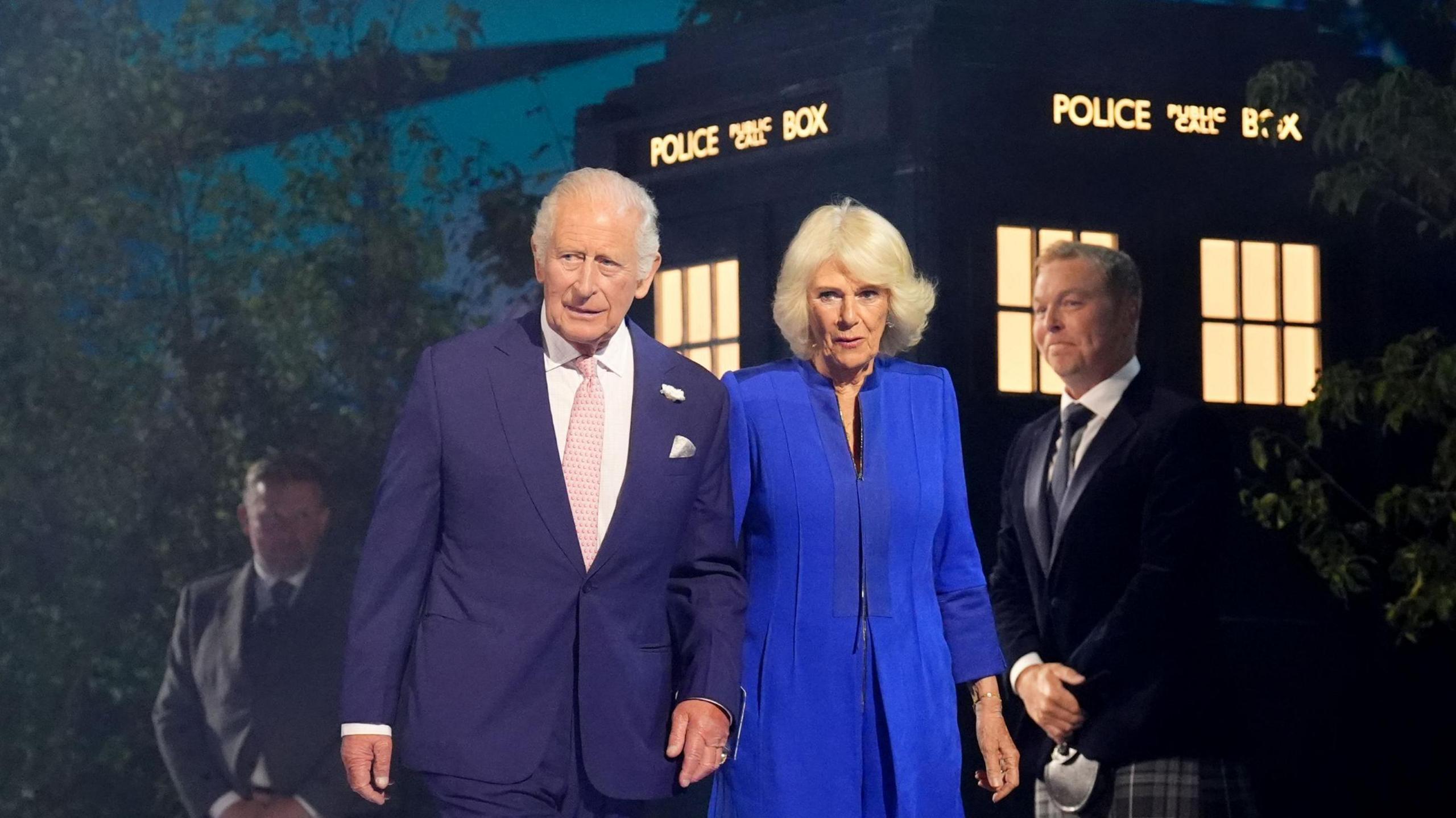 The King and Queen are walking in front of a Tardis. Sir Chris Hoy is standing behind them.