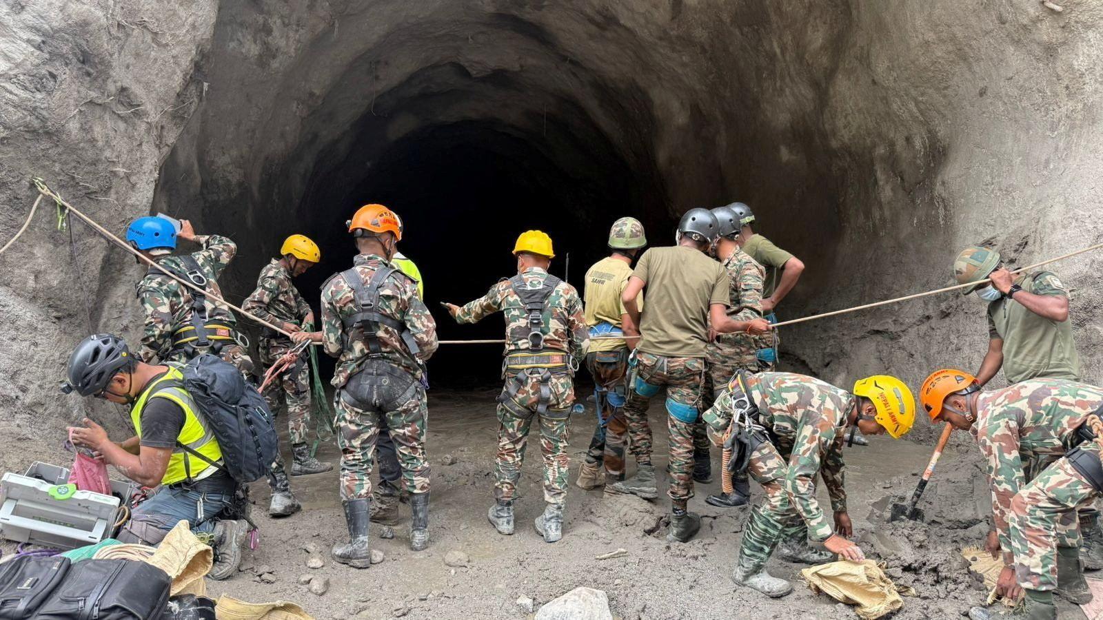 People in camouflage clothing and wearing helmets stand at the entry to a tunnel