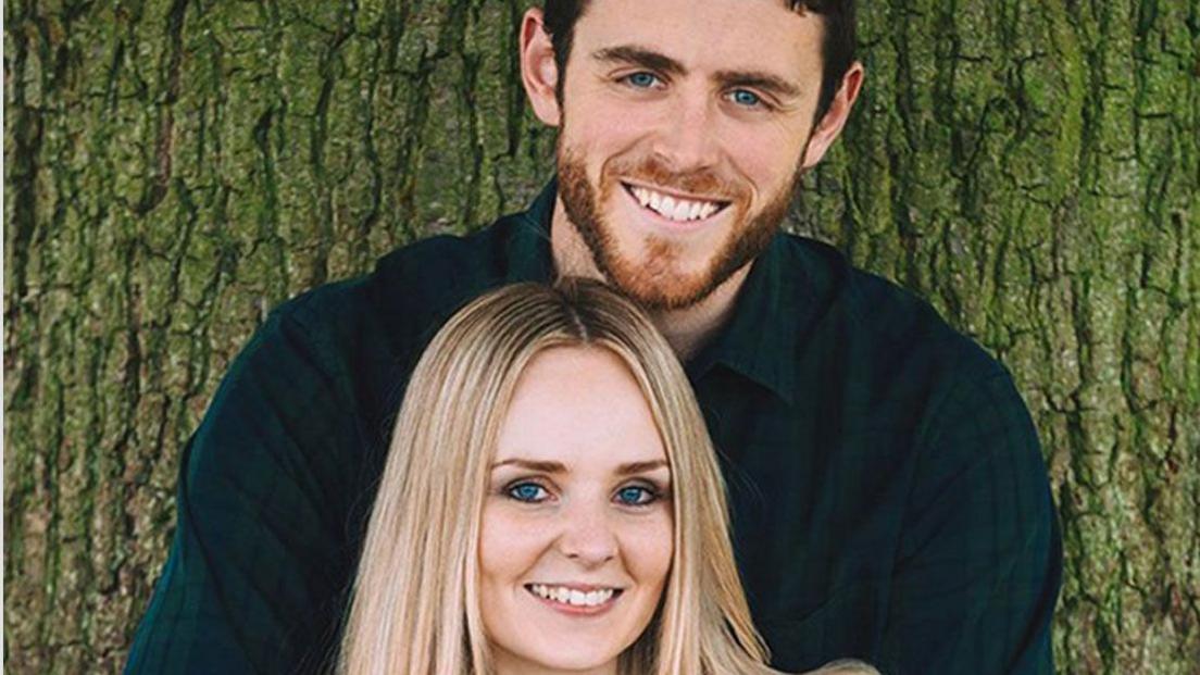 Police officer Andrew Harper, off duty, clasps his hands around his wife, Lissie, who puts her hands over his. They are both facing the camera, smiling.