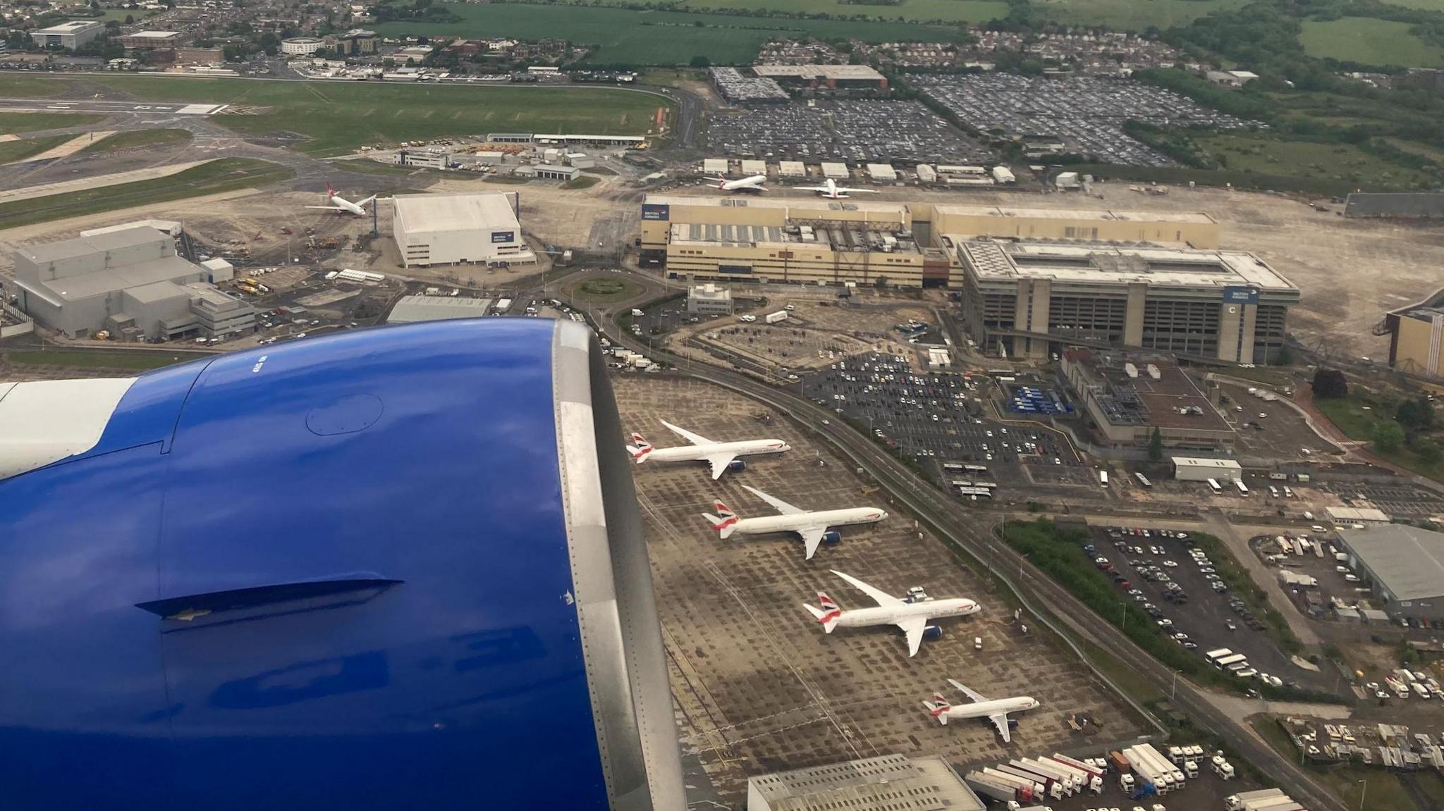 View from a plane shows blue engine of plane and four aircraft on tarmac outside low-rise terminal buildings.
