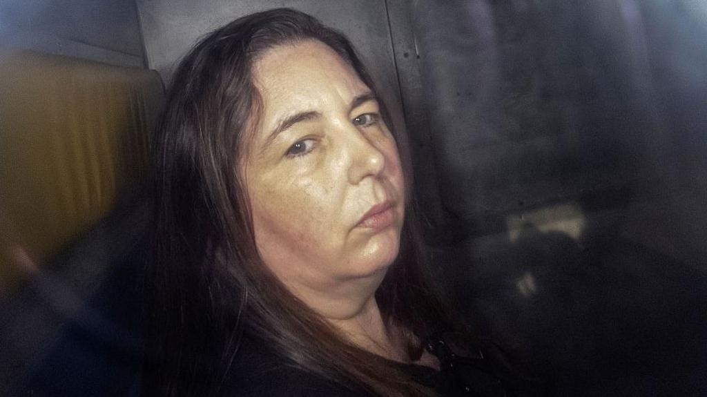 Erin Patterson looks at the camera from the back of a police van