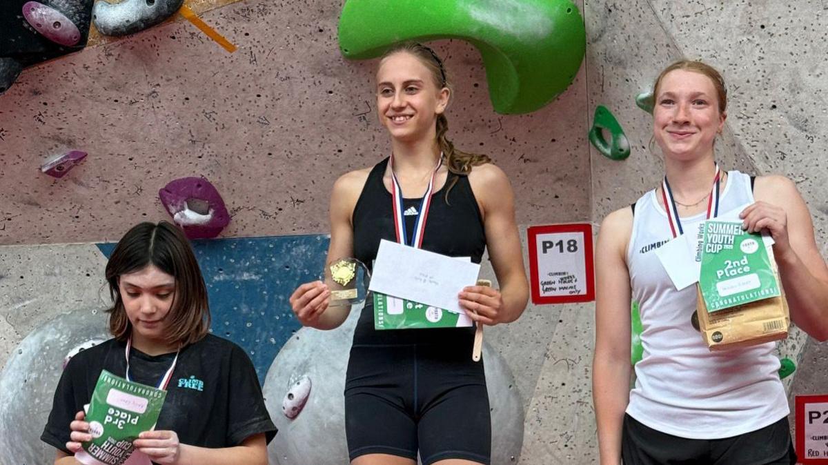 Mary Falconer with a gold medal on top of a climbing podium