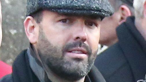Daniel Kinahan, a man with short dark hair and a stubbly beard, pictured at a funeral in 2016.  He is wearing a grey peaked cap, a black shirt and a black coat with the collar pulled up.