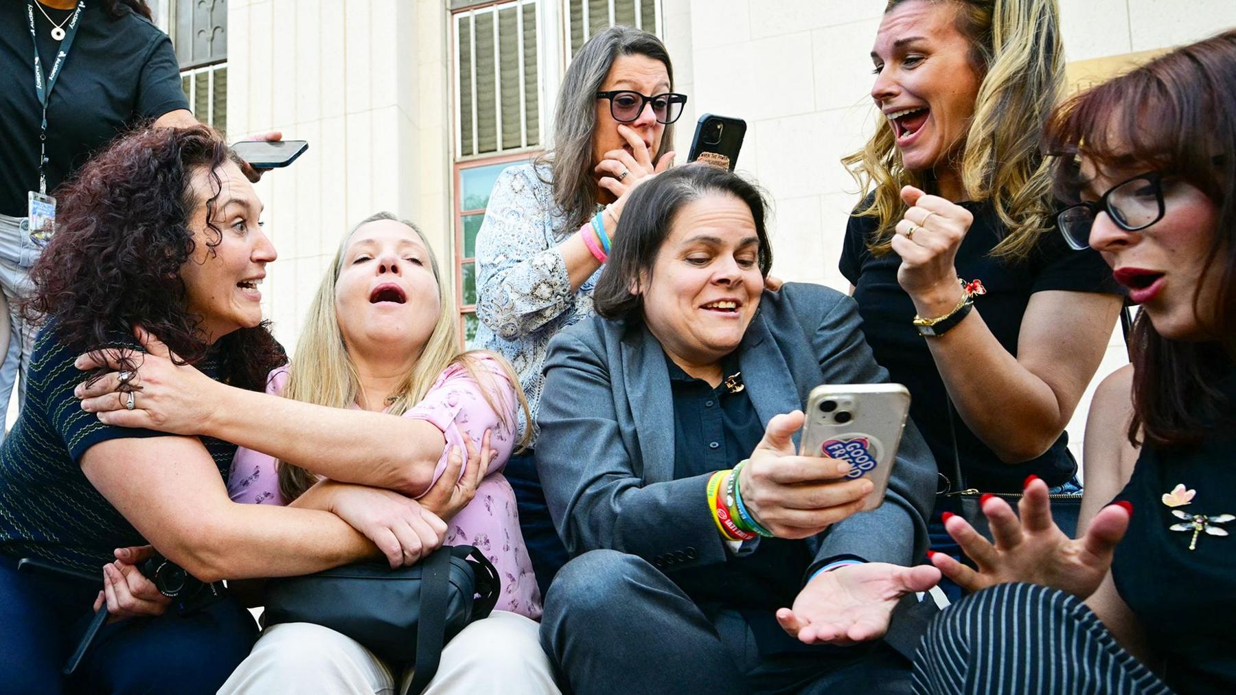A group of women sit on steps in front of an Los Angeles courthouse and react with happiness and tears at verdict