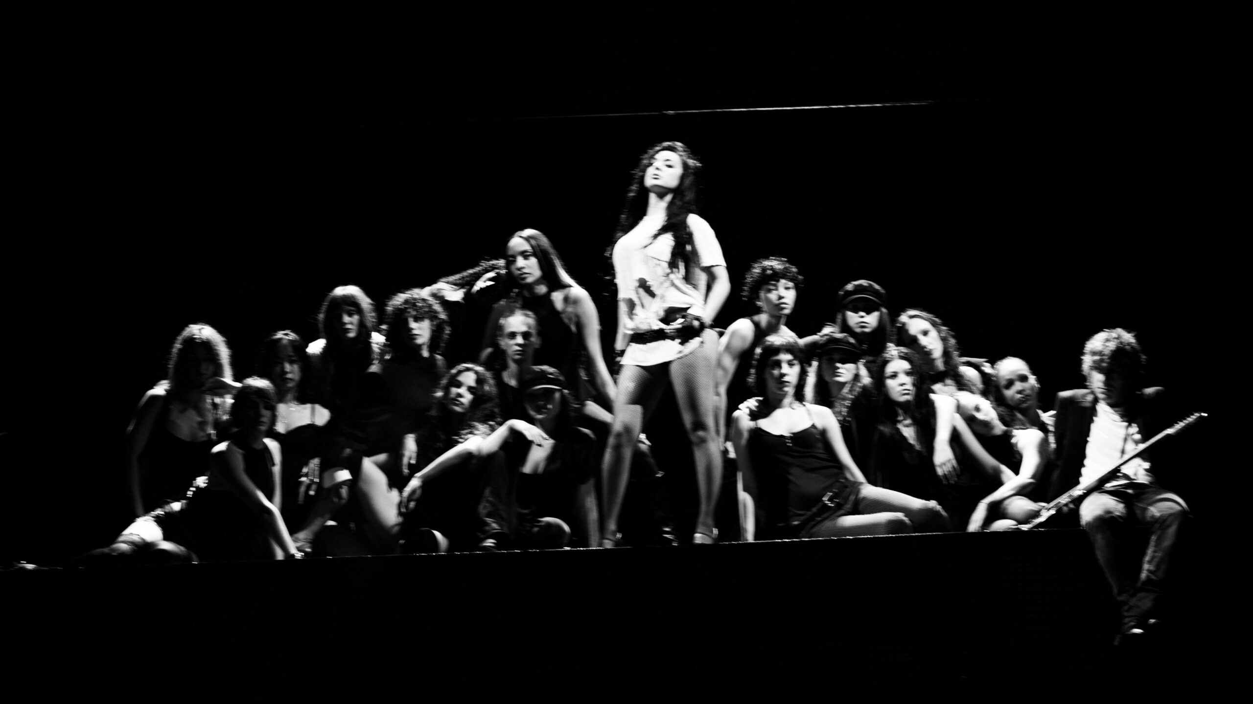 A black and white photo of Charli XCX as she stands on stage surrounded by dancers.