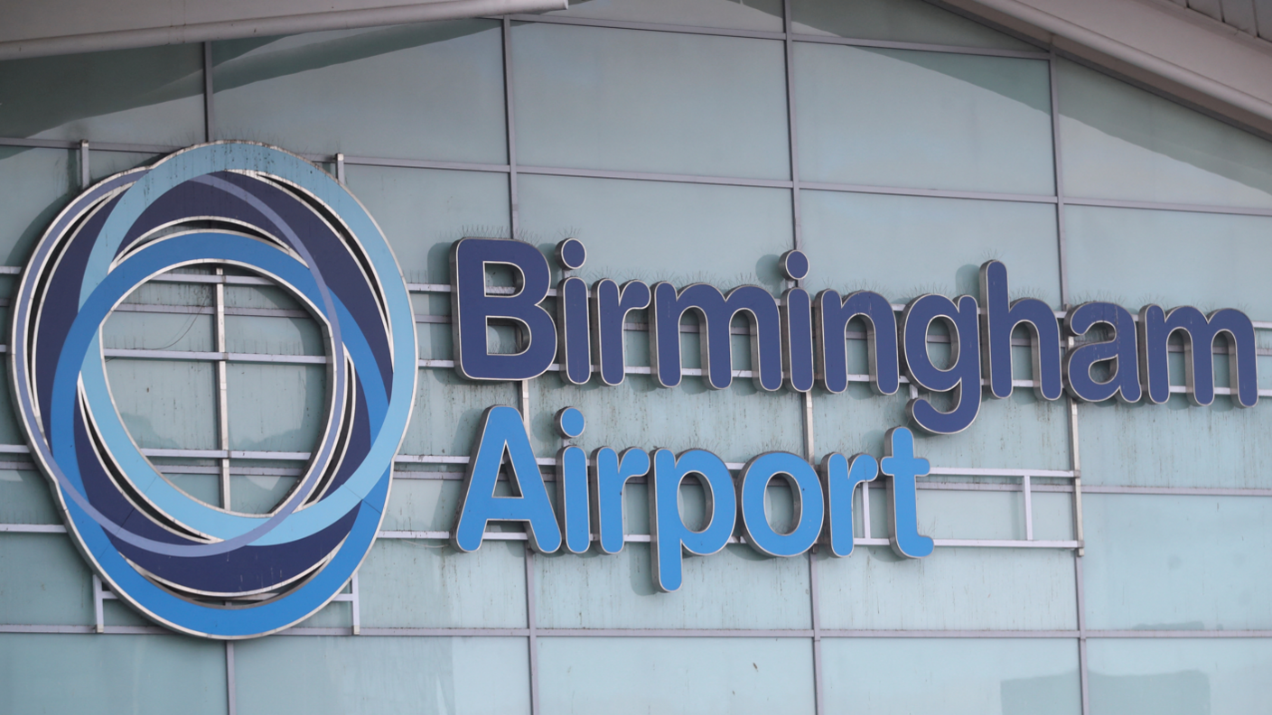 Birmingham Airport is written on the side of a building with a fogged glass exterior. The words are in dark blue and light blue lettering and there is a circular symbol to the left of the words.