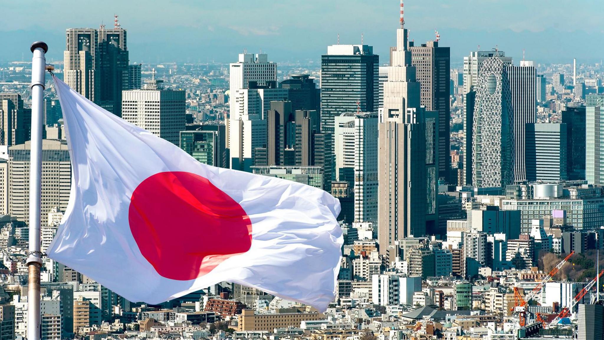A Japanese flag flies in front of the Tokyo skyline