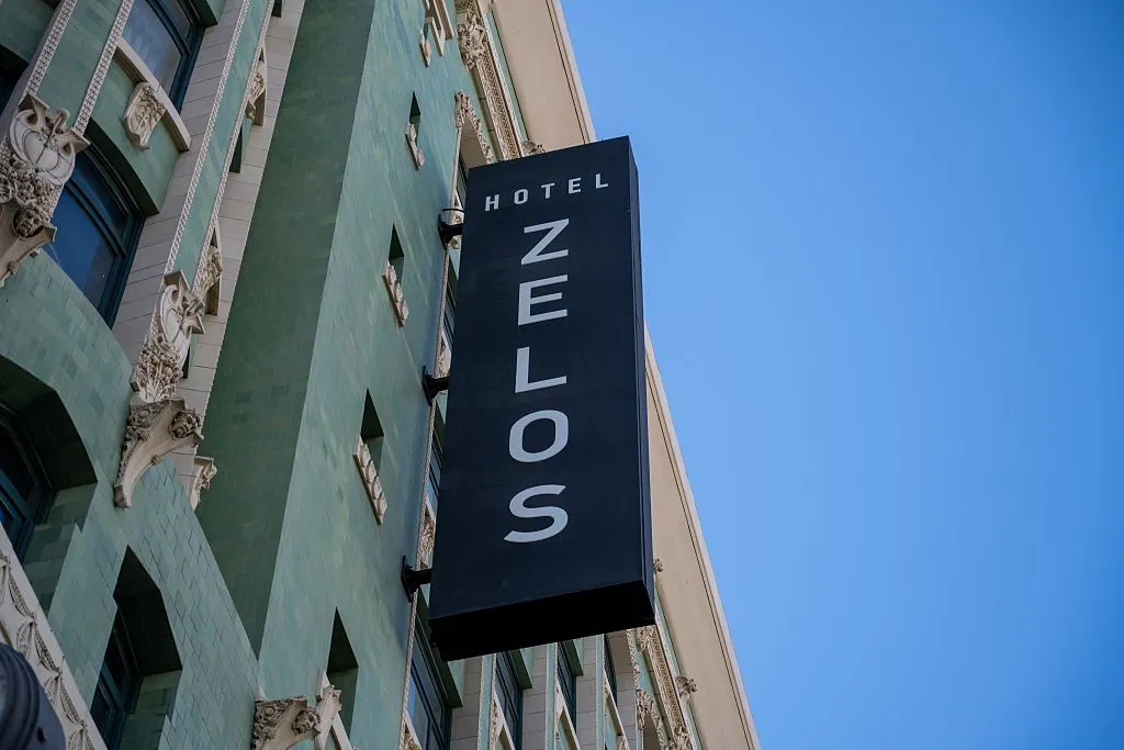 Vertical sign for Hotel Zelos on green tiled historic facade under clear blue sky, San Francisco, California, August 19, 2025.