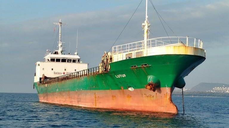 The MV Lutuf anchored close to the shore. The green and orange hull can be seen above the water.