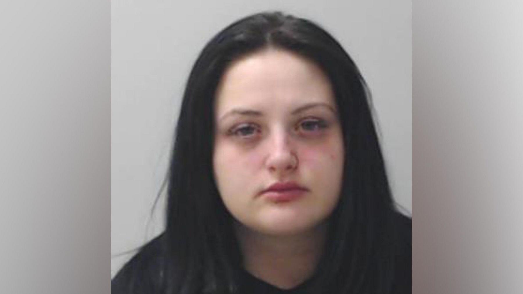 A mugshot of a young woman with long dark hair, looking at the camera.