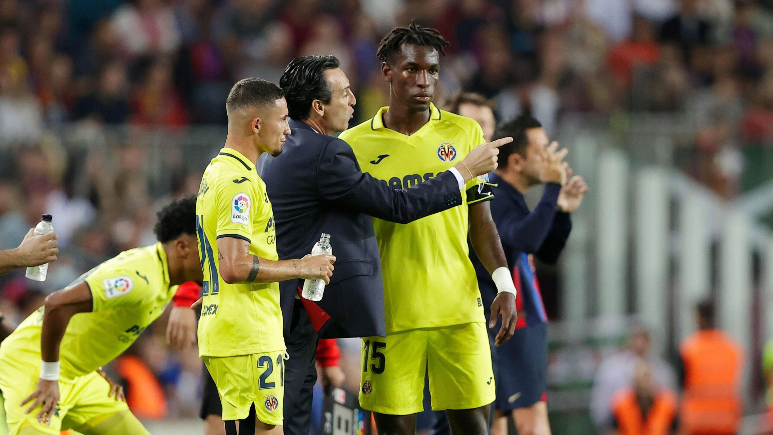 Villarreal manager Unai Emery, in a black suit, talks with Nicolas Jackson and Yeremi Pino - both wearing the club's yellow kit - on the touchline during a La Liga match against Barcelona
