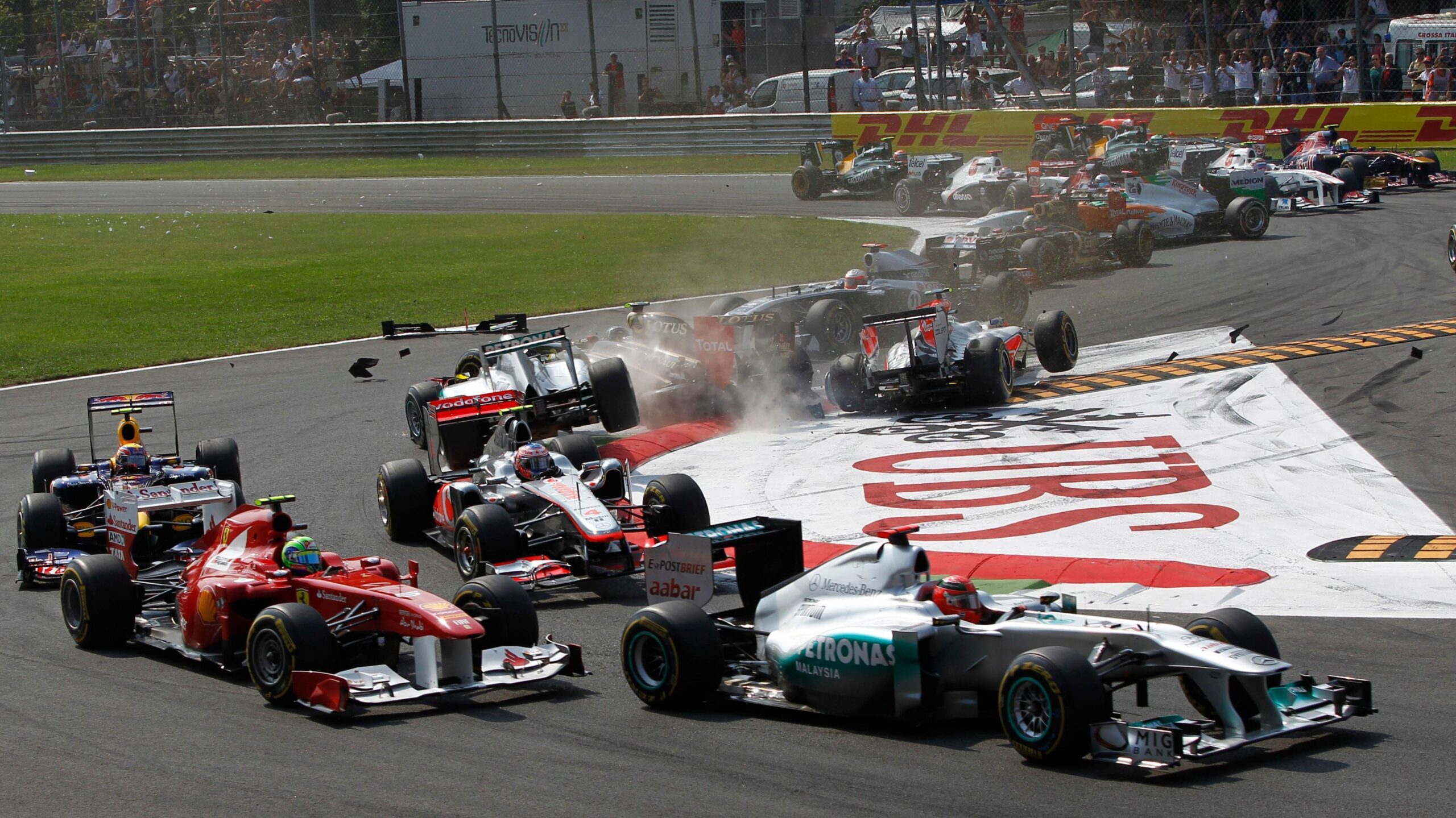 Michael Schumacher, driving a Mercedes, is at the front of the pictures as the field goes through the first chicane in the 2011 Italian Grand Prix. A number of cars are facing the wrong way after contact with competitors and debris can be seen on the track