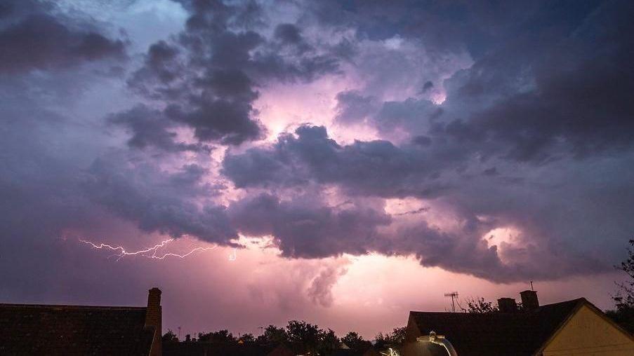 Skyline photo with dark clouds illuminated by forks of lightning, above rooftops