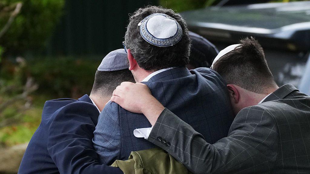 Three men wearing Jewish skullcaps - kippahs - seen from behind as they embrace, with their arms around each other
