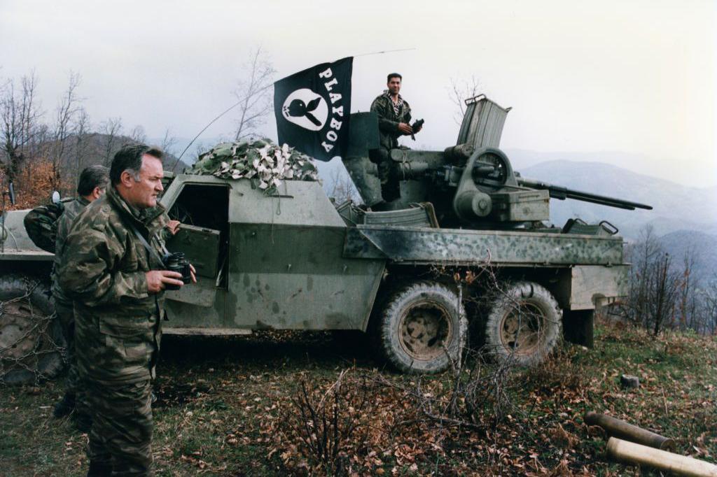 General Mladić leads his troops in 1994. He is standing next to a military vehicle and he is holding binoculars