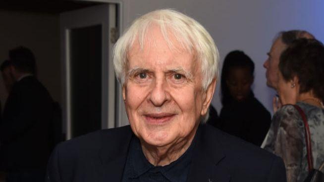A man with white hair looks at the camera