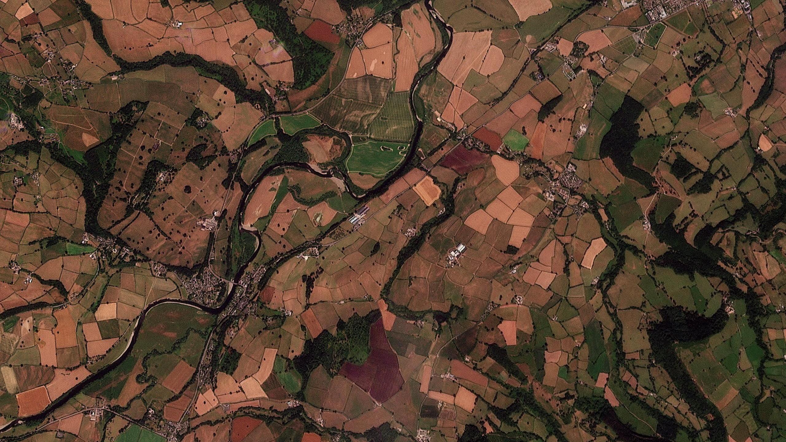A birdseye view of a patchwork of brown, red and infrequent green fields in England and Wales