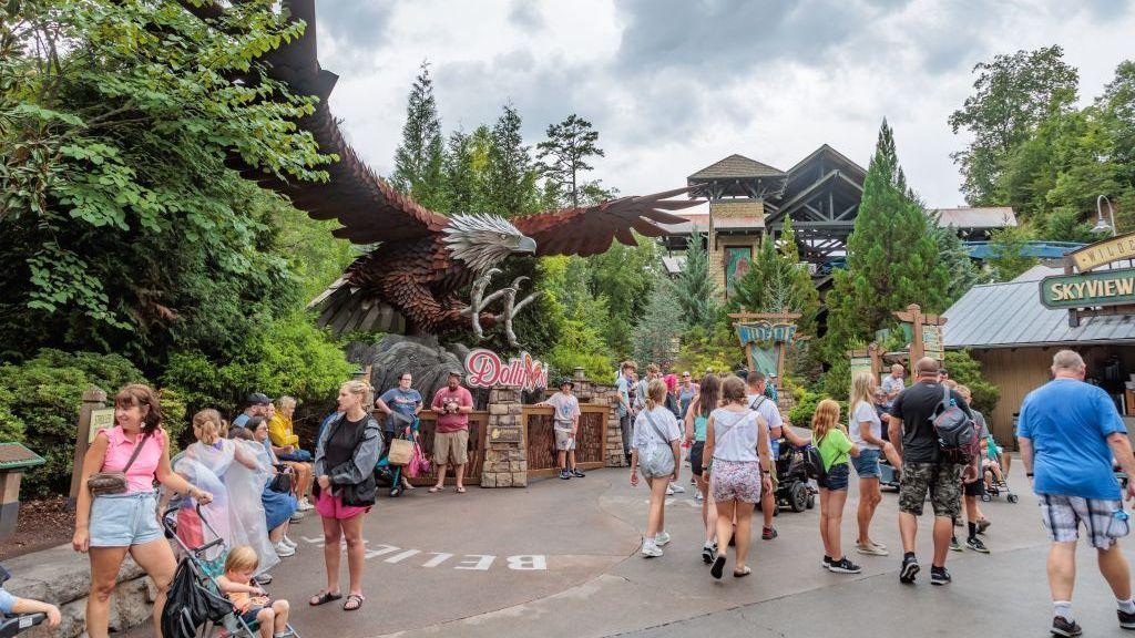 A large statue of an eagle with spread wings is in the midst of a theme park swarming with visitors