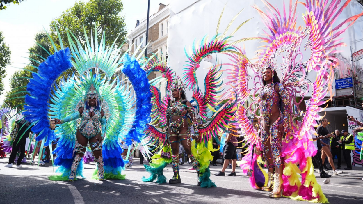 Three women in feathered and beaded costumes pose on a London road.