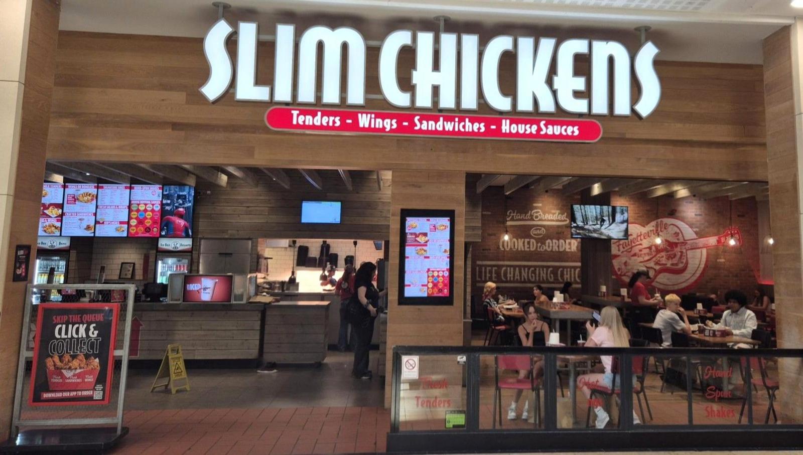 A Slim Chickens store inside a shopping centre with shoppers walking past.