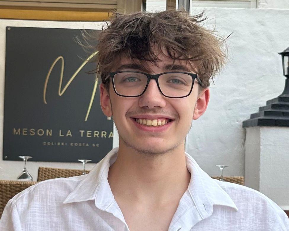 A man in a white shirt and dark glasses smiles