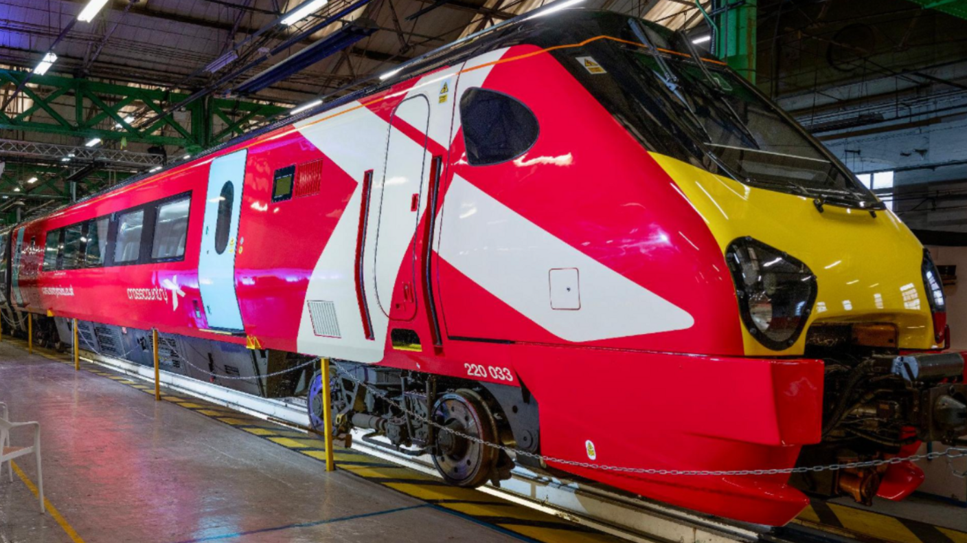 An image of a refurbished CrossCountry Voyager train inside a warehouse at a launch event. The train is mainly red, with a white X, which is partially on the driver's door.