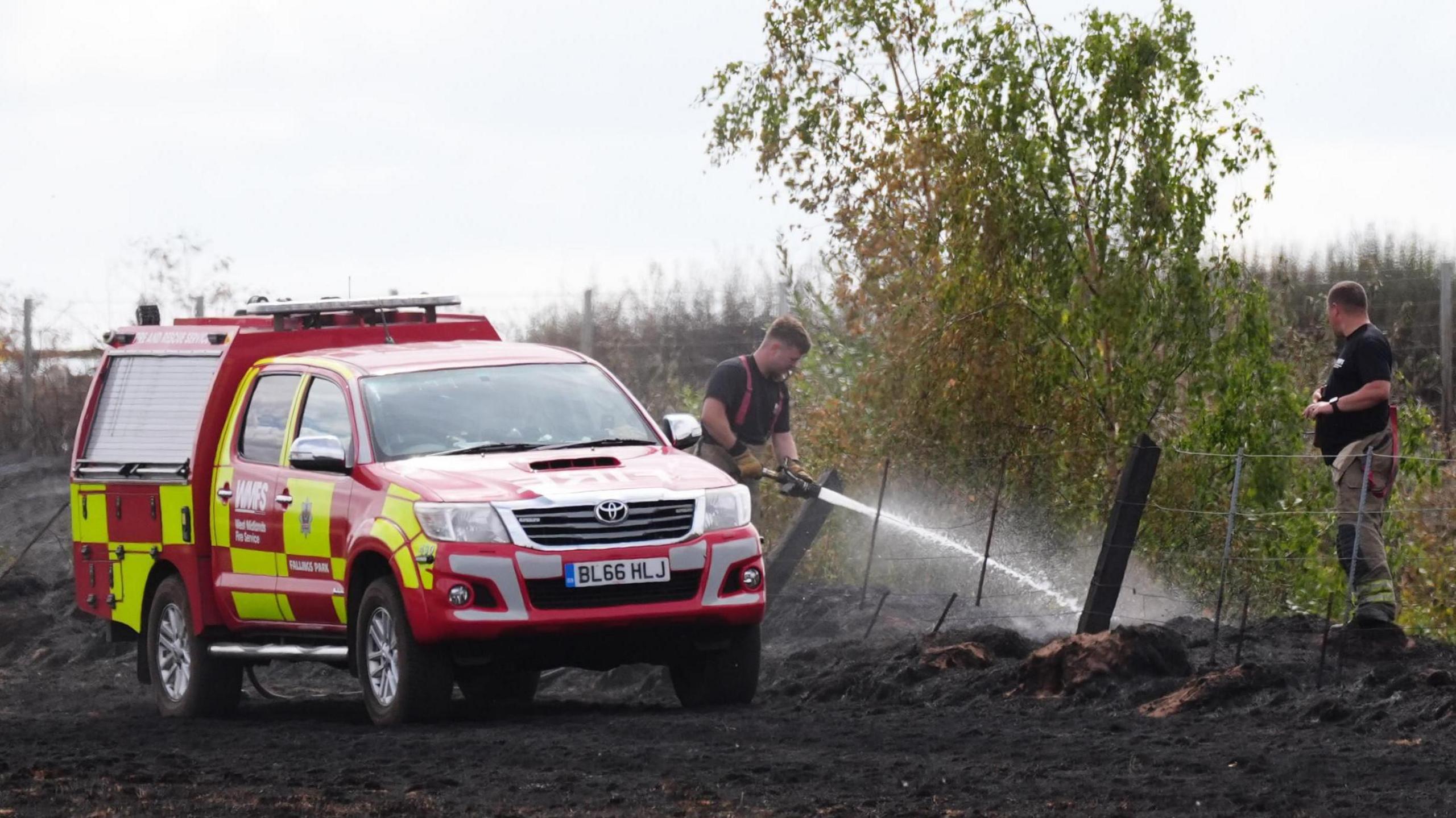 Firefighters dampen down a field next to burnt out houses