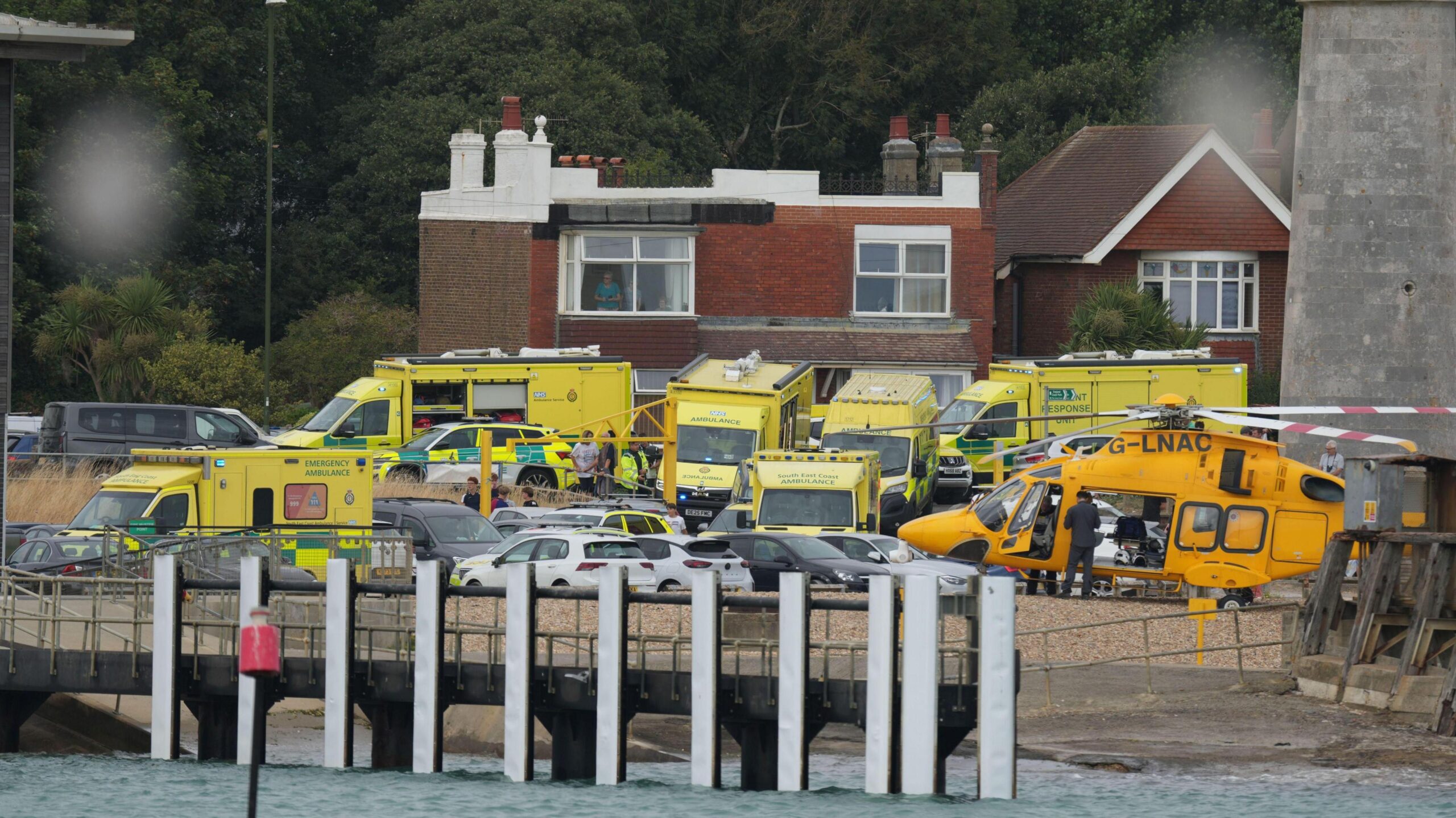 Ambulances, emergency response vehicles and an air ambulance helicopter are gathered near the seafront during an emergency operation.