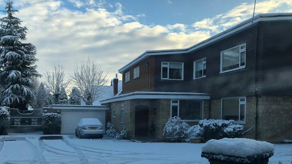 A two storey home with a large garden and a car parked in front of a garage, all covered in snow