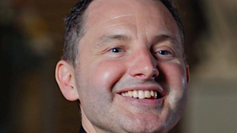 Father Frankie Mulgrew is a middle-aged man with short dark hair which is greying at the sides. He is looking off to the left slightly and is smiling broadly.