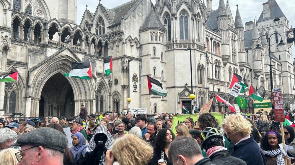 General view of people stood outside the Royal Courts of Justice building in London. A number of Palestinian flags can be seen