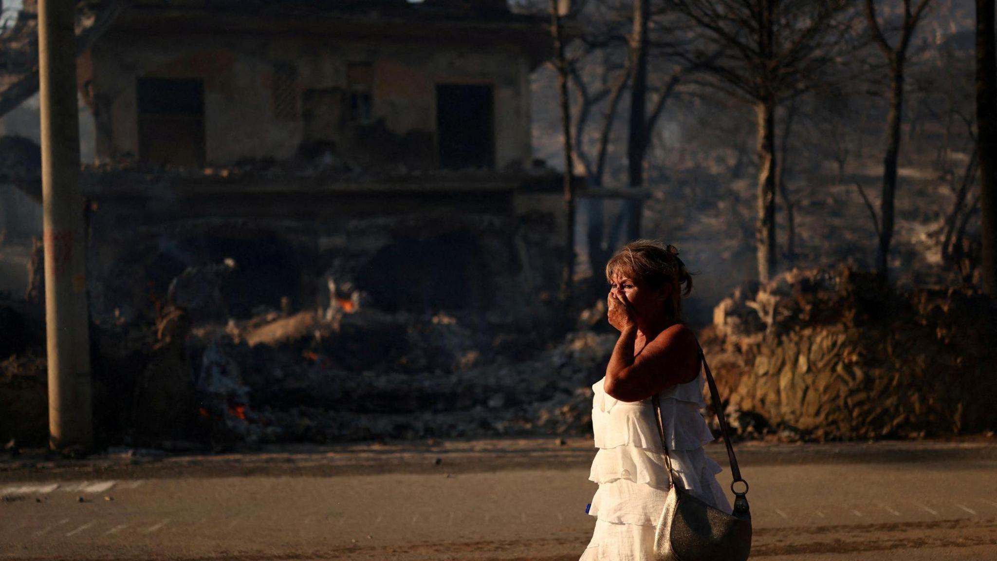 A woman walks near a burnt house during a wildfire on Salamina island, near Athens, Greece