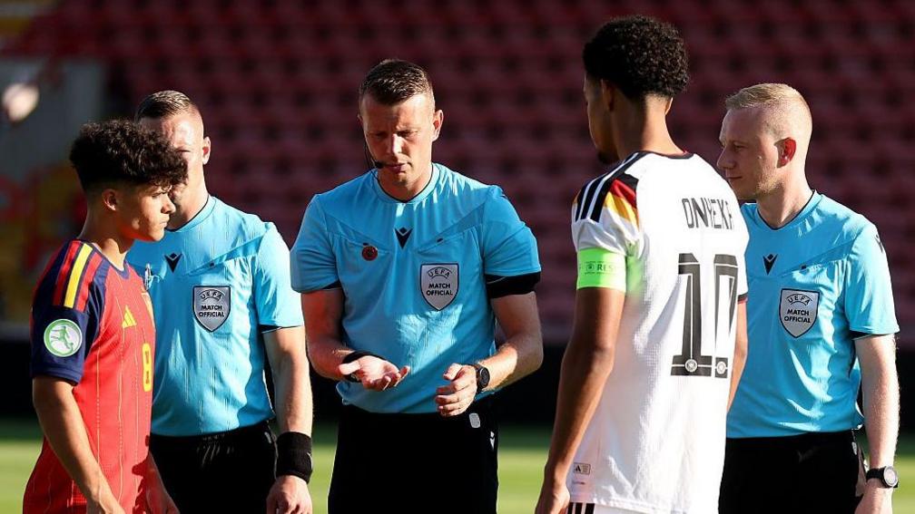 Sam Barrott tossing a coin in front of the captain of Span and Germany before the Under-19 European Championship final