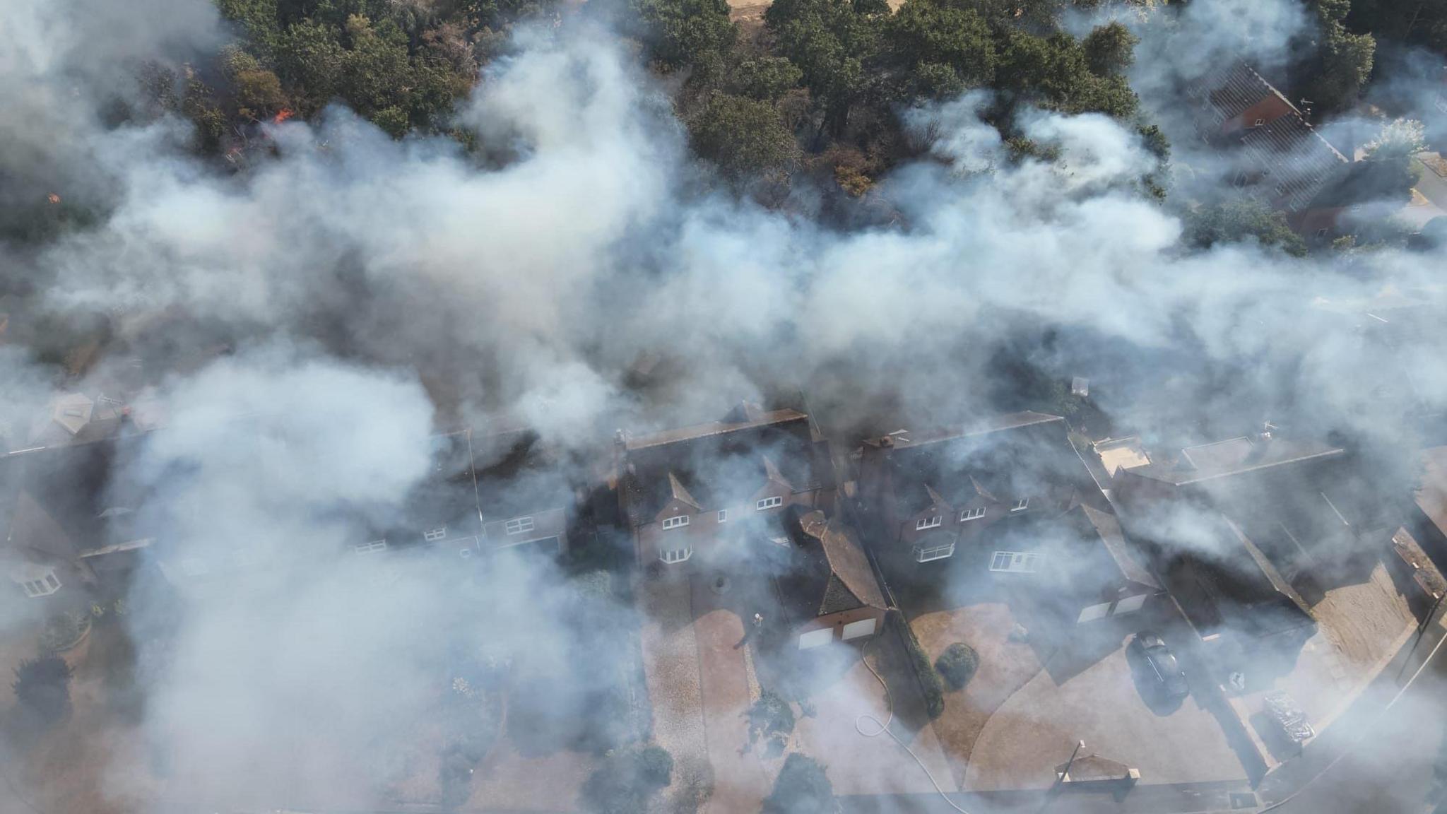 An aerial photo of grey smoke hanging above houses with trees behind.