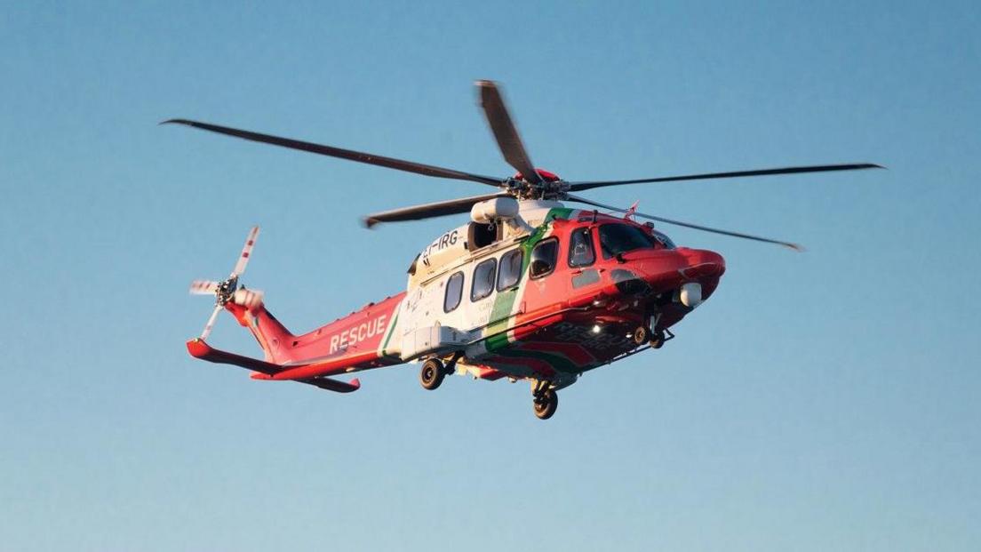 A red and white Irish Coast Guard helicopter flying in a clear blue sky.