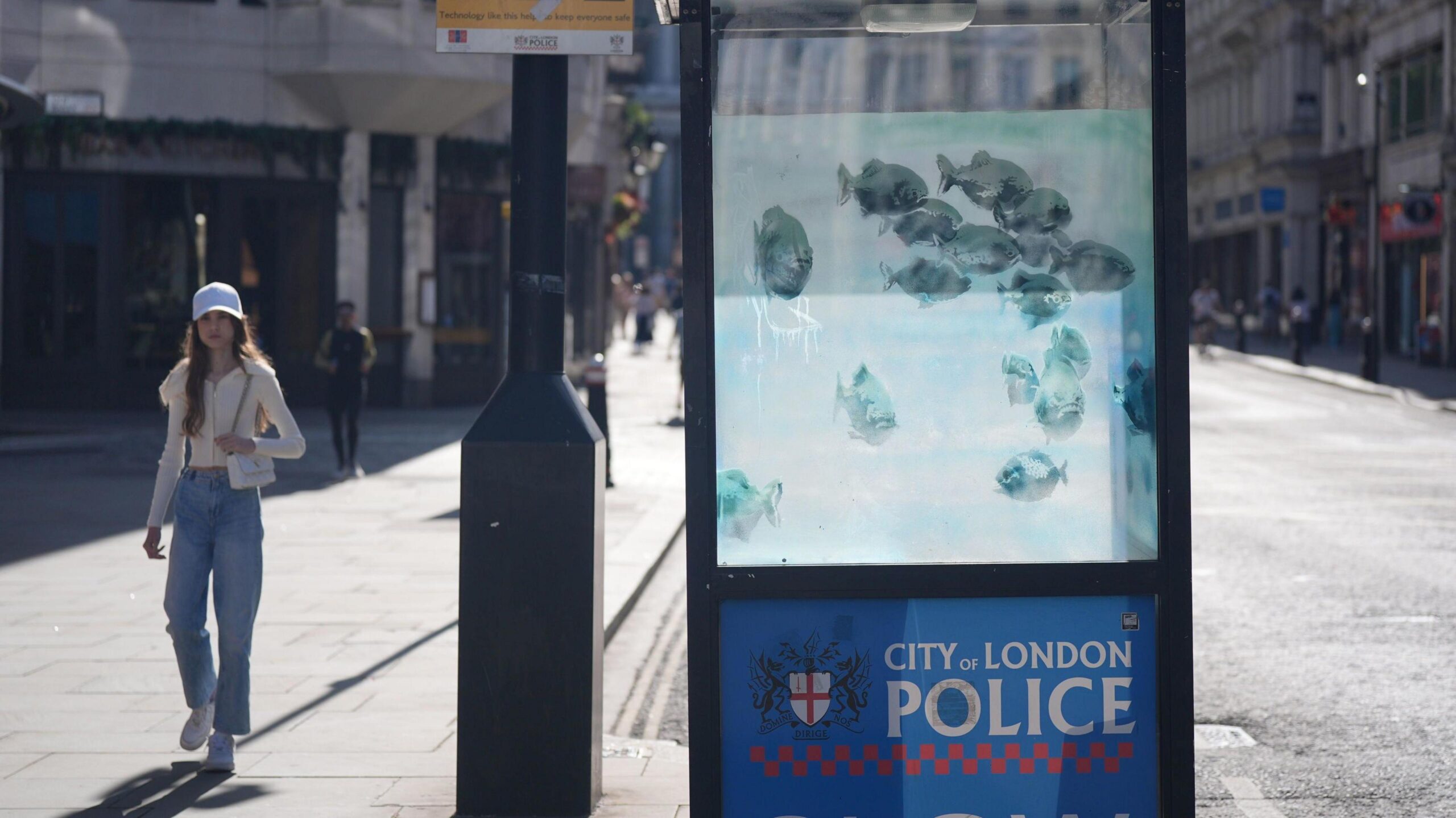 A woman walks past a City of London Police sentry box that has had its perspex windows painted with Piranha fish.