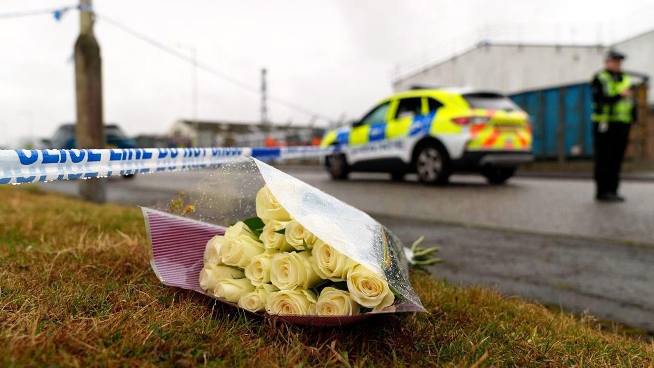 A bouquet of yellow roses placed on the ground with a police cordon in the background