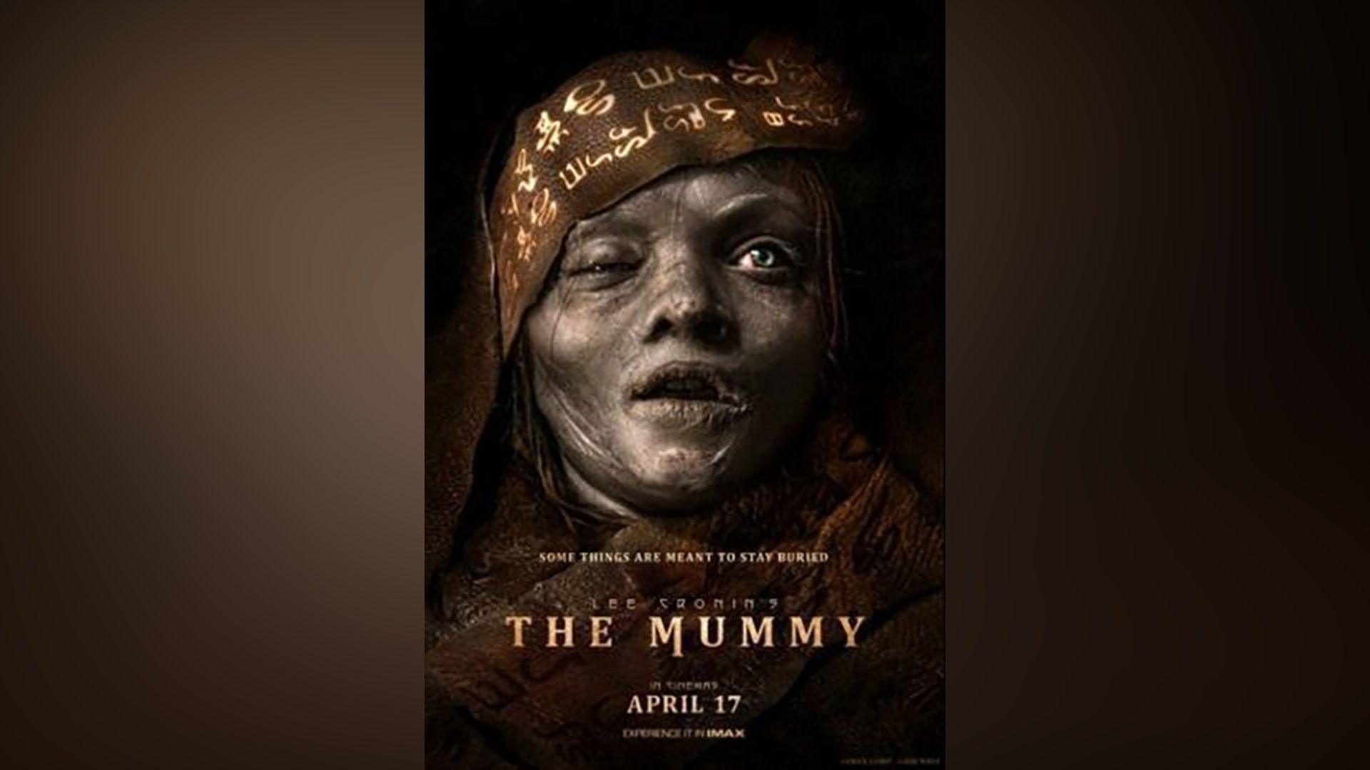 A dark movie poster showing a close-up of a mummified figure with grey, decaying skin, cracked lips, and one eye swollen shut. The head is wrapped in patterned fabric covered in symbols. Text across the bottom reads: "Some things are meant to stay buried. Lee Cronin's The Mummy. In cinemas April 17."
