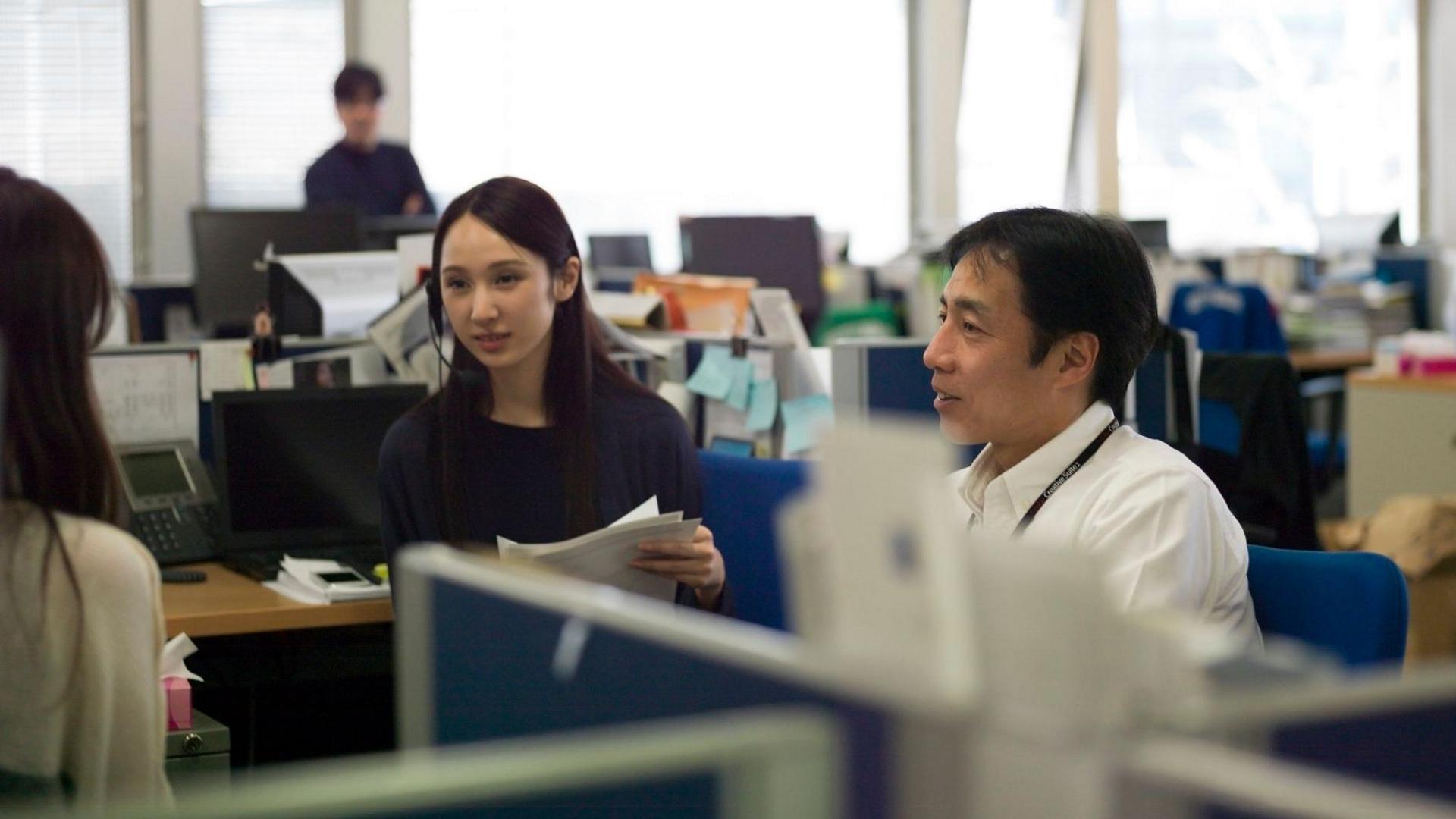 A posed scene from a Japanese office, with three workers having a meeting
