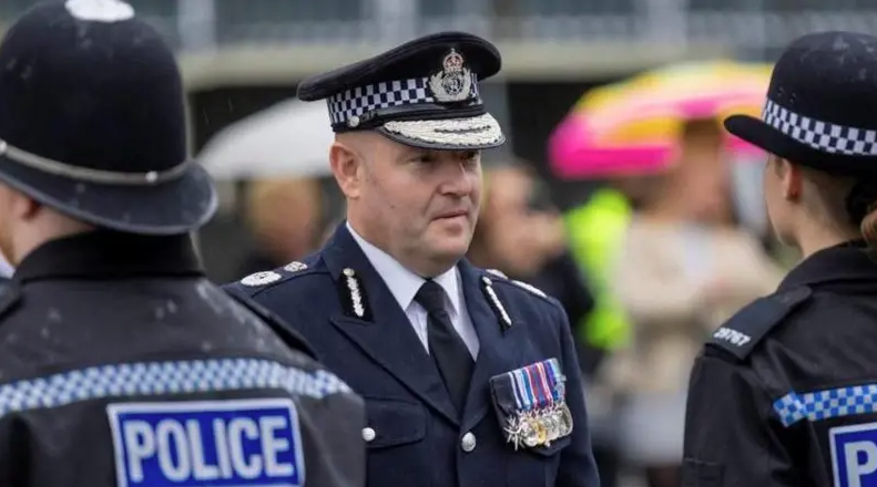 Craig Guildford, a man wearing ceremonial police uniform, looks at a line-up of police officers who are dressed in full police uniform.