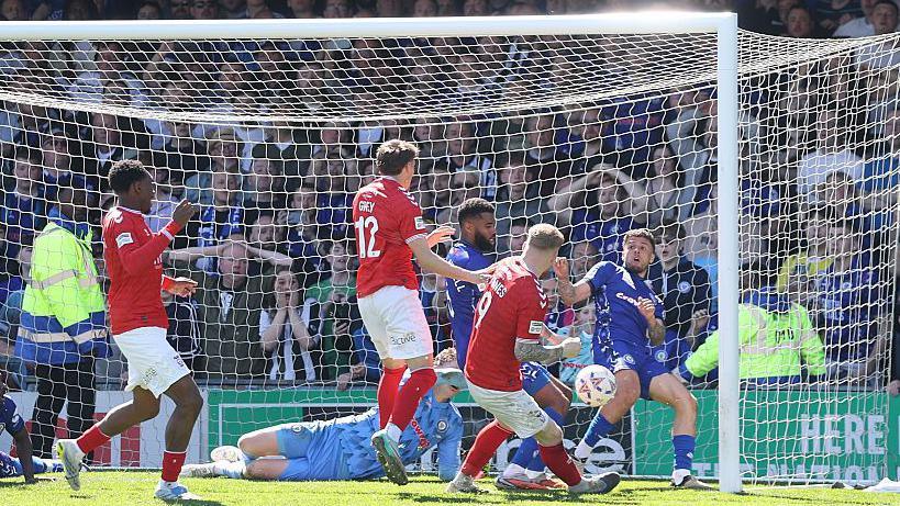 Josh Stones, in a red York City shirt, stabs the ball past Rochdale defenders on the goal-line