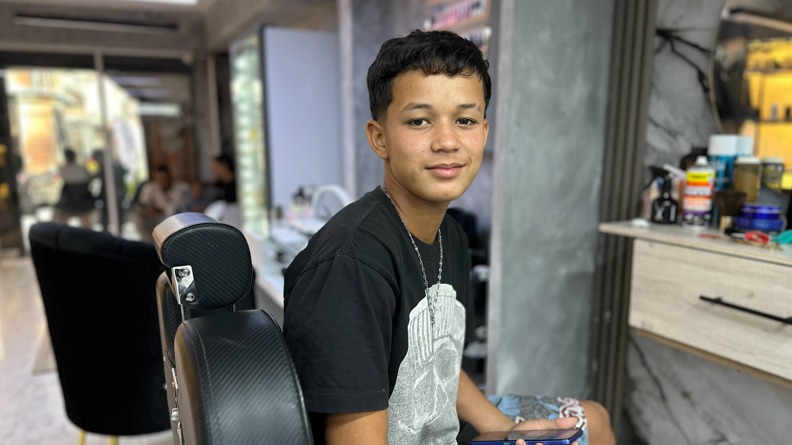 Deivi Delfín sits in a barber's shop
