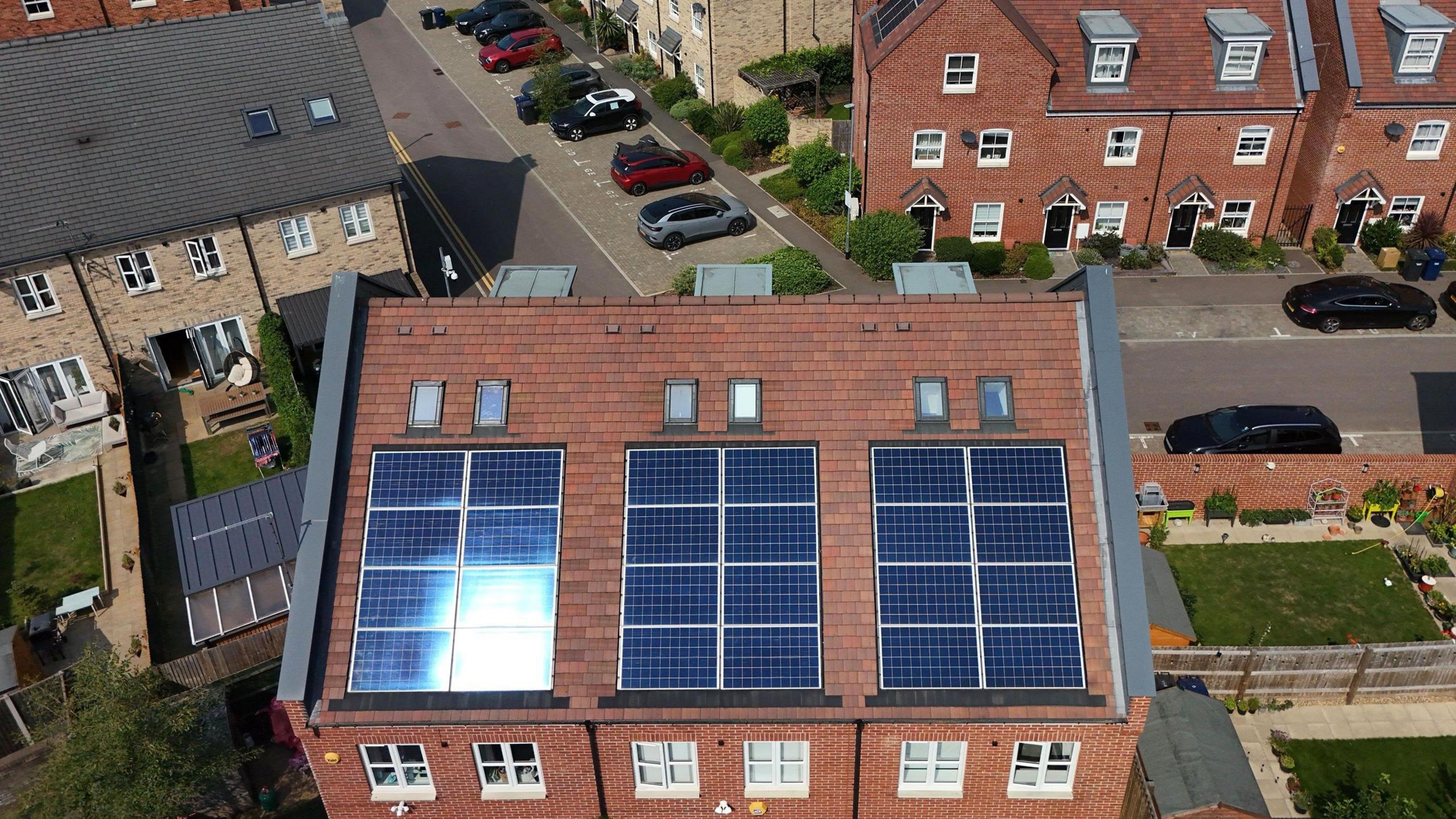 Aerial view of semi-detached and homes and terraced houses with solar panels installed. In the background are a series of avenues with cars parked up and small green lawns.