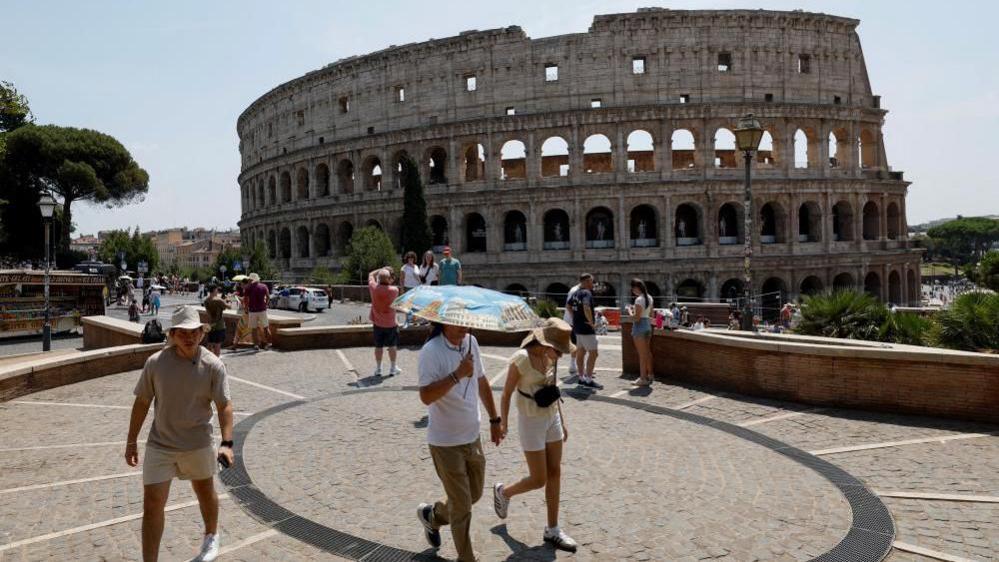 A person holds an umbrella as people walk near the Colosseum during a heatwave across Italy, as temperatures are expected to rise further in the coming days, in Rome, Italy August 3, 2026.