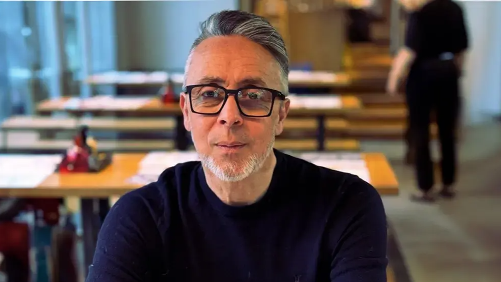 Simon Gooch, with quiffed black and grey hair, wears a blue crew neck jumped.