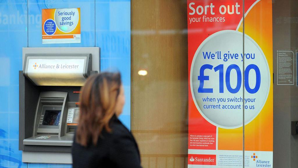 Woman wearing a dark coat looks at a sign that reads: Sort out your finances. We'll give you £100 when you switch your current account to us.
