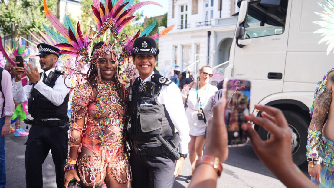 A woman in a pink beaded costume poses for a photograph with a Met Police officer.
