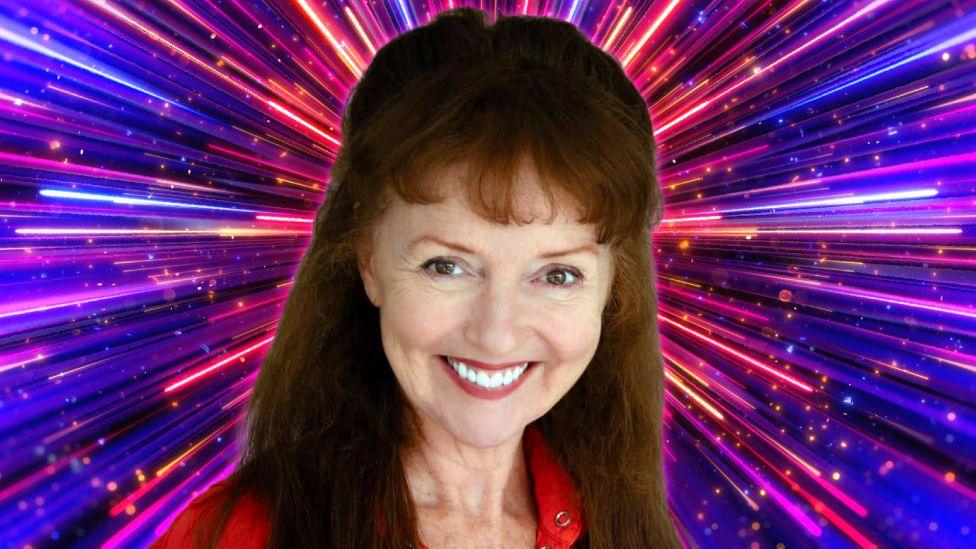 Melanie Walters smiling and wearing a red top, with the pink and purple Strictly Come Dancing background